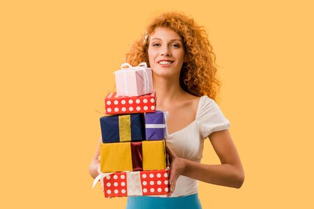 attractive redhead girl holding gift boxes isolated on yellow
