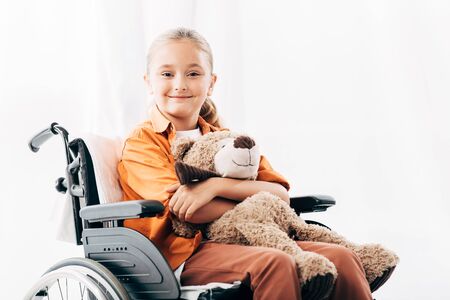 smiling kid holding teddy bear and sitting on wheelchairの写真素材