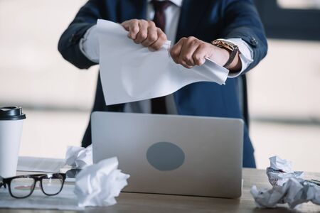 cropped view of businessman tearing paper in officeの写真素材