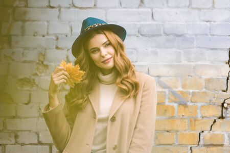 attractive woman in blue hat looking at camera and holding yellow leavesの写真素材
