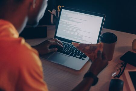 cropped view of young african american programmer eating pizza while working at night in office