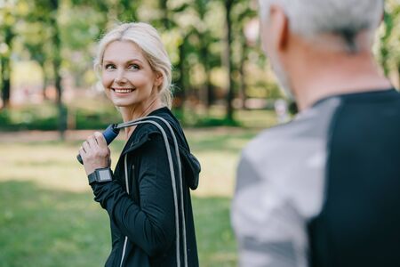 selective focus of smiling sportsman with jump rope looking at mature sportsmanの写真素材