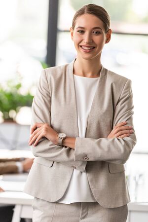 front view of confident businesswoman in formal wear standing with crossed arms in officeの写真素材