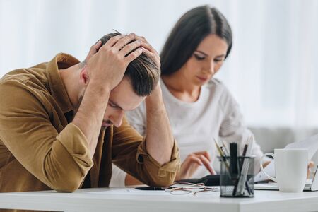 sad and handsome man holding head and attractive woman using calculator