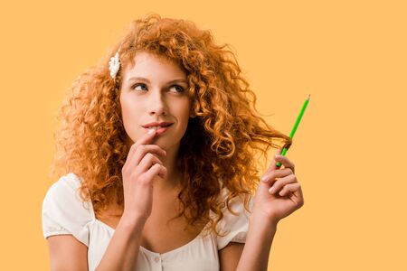 attractive thoughtful woman with pencil isolated on yellowの写真素材