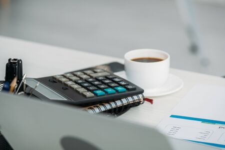 selective focus of cup with coffee, calculator and notebooksの写真素材