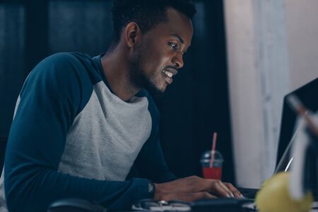 smiling african american programmer sitting at workplace at night