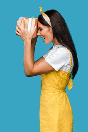happy woman in headband holding books near head isolated on blueの写真素材