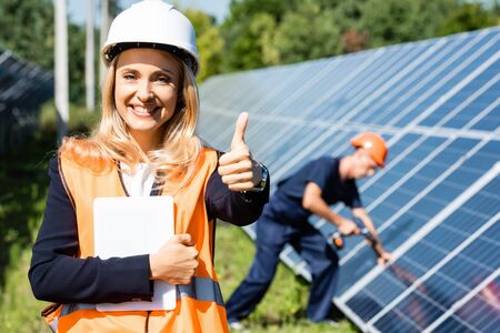 attractive businesswoman in hardhat showing thumb up and holding digital tabletの写真素材
