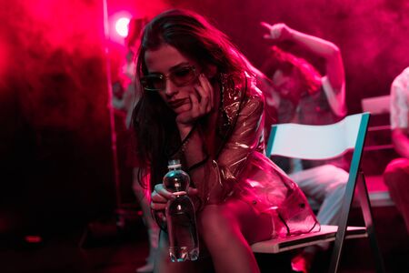 sick young woman sitting with bottle of water in nightclubの写真素材