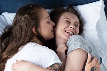 two smiling lesbians embracing while lying in bed
