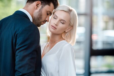 bearded man with closed eyes flirting with beautiful blonde coworker in officeの写真素材