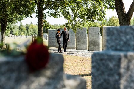 selective focus of man and woman walking near tombstones in cemetery