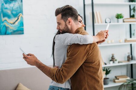handsome man hugging with attractive woman and using smartphonesの写真素材