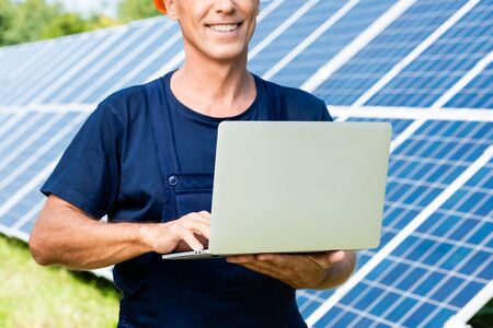 cropped view of engineer in t-shirt smiling and holding laptop
