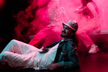smiling man lying on floor in nightclub during rave party with pink smoke