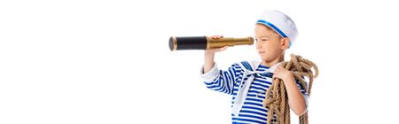 panoramic shot of focused boy in sailor costume holding rope and looking through spyglass isolated...