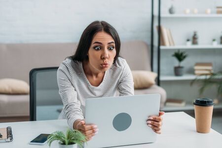 beautiful and brunette woman looking at screen of laptop and making faces