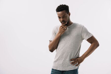 pensive african american man standing with hand on hip and touching face isolated on white