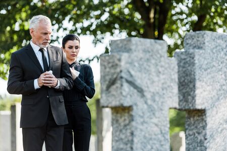 selective focus of senior man and attractive woman on graveyard