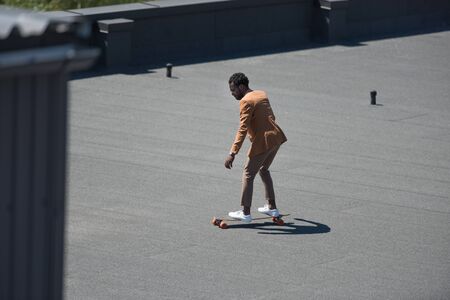 african american businessman riding longoard on sunny rooftopの写真素材