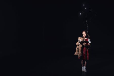 depressed, lonely child holding black balloons and teddy bear isolated on blackの写真素材