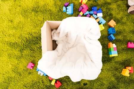 Top view of cardboard box with white blanket and colorful pieces of construction
