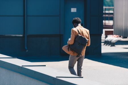 back view of stylish african american businessman with bag walking on rooftop