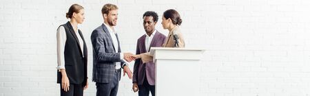 panoramic shot of four multiethnic colleagues in formal wear talking and shaking hands