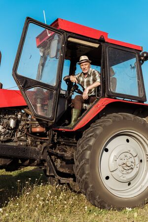 senior self-employed farmer in straw hat driving tractor