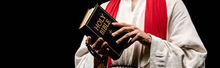 panoramic shot of man holding book with holy bible letters isolated on blackの写真素材