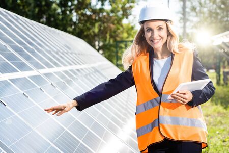 businesswoman in safety vest and hardhat smiling and holding digital tablet