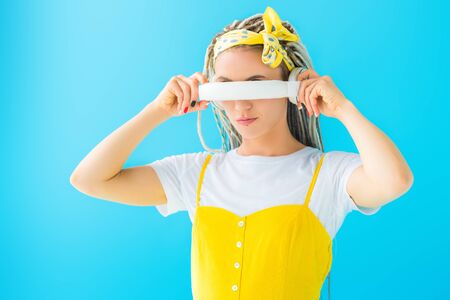 girl with dreadlocks covering face with headphones isolated on turquoise