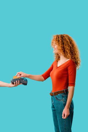 curly redhead woman paying with credit card on terminal, Isolated On blue