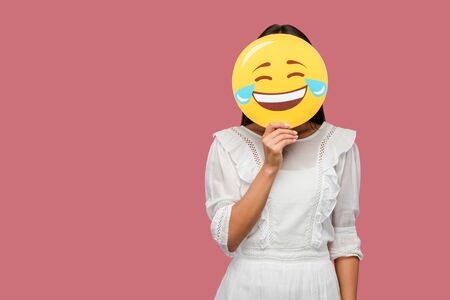 woman covering face with smiley isolated on pinkの写真素材