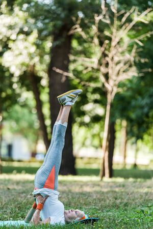 retired woman in sportswear exercising on fitness mat near treesの写真素材