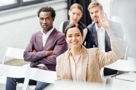 selective focus of attractive woman in formal wear raising hand during conference