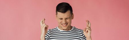 panoramic shot of front view of smiling man in striped t-shirt with closed eyes and crossed fingers...