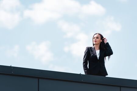 attractive businesswoman standing on rooftop, smiling an looking awayの写真素材