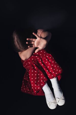scared, lonely child sitting with outstretched hand on black backgroundの写真素材