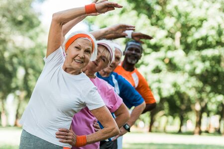 selective focus of cheerful retired woman near multicultural men and woman doing stretching exercise