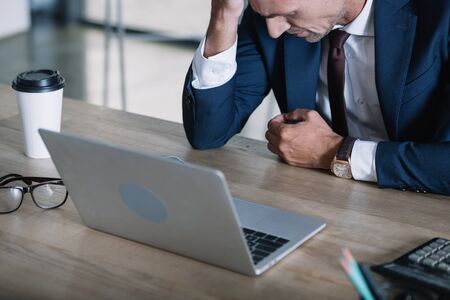 upset businessman near laptop and paper cup in officeの写真素材