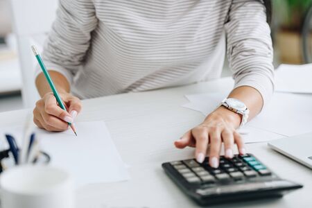cropped view of woman using calculator and writing with pencil