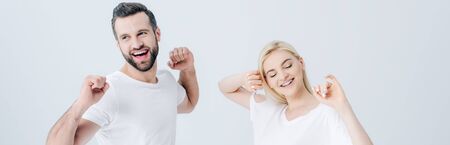 panoramic shot of happy man and young woman stretching with clenched fists isolated on grey