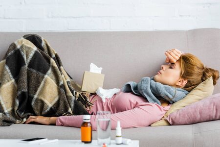side view of attractive and ill woman in grey scarf with headache lying in apartmentの写真素材
