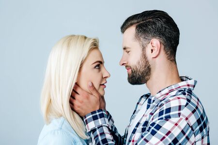 handsome man embracing face of beautiful young woman isolated on grey