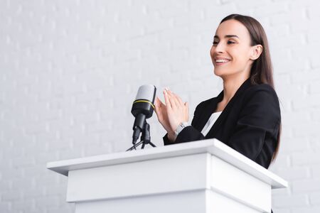 happy speaker clapping hands while standing on podium tribune in conference hallの写真素材