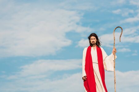 handsome bearded man holding wooden cane and standing outside