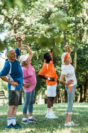 selective focus of cheerful multicultural senior men and women standing with hands on hips while...