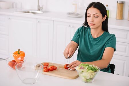 pretty, young disabled woman cutting tomatoes on chopping board in kitchenの写真素材